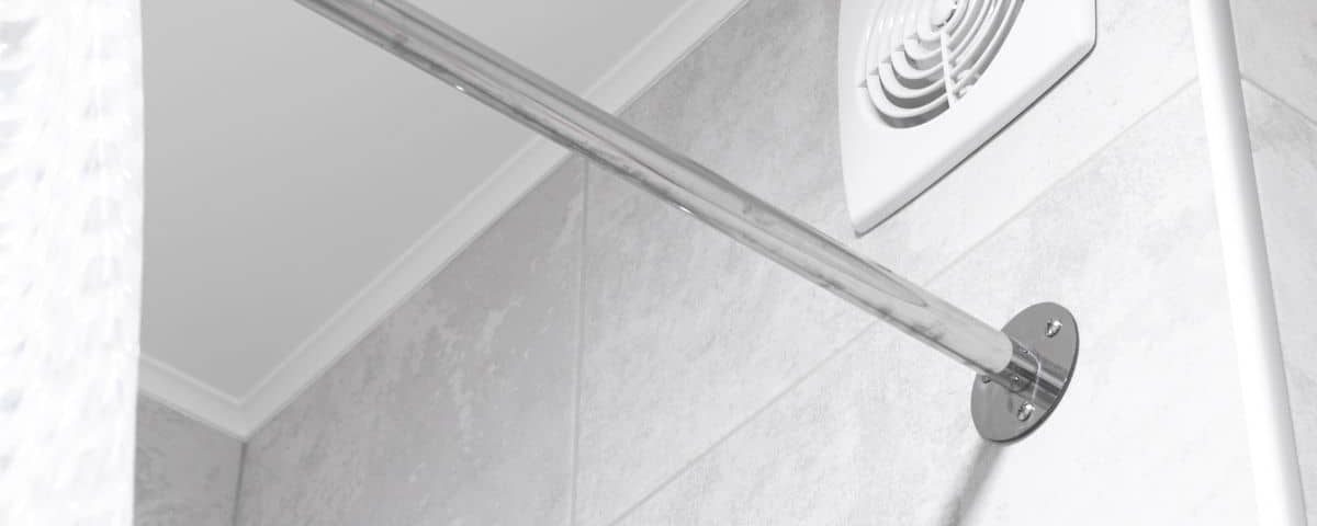 Bouche d’extraction d’air blanche fixée en haut du mur carrelé d’une salle de bains, au-dessus d’une douche.