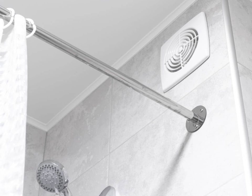Bouche d’extraction d’air blanche fixée en haut du mur carrelé d’une salle de bains, au-dessus d’une douche.